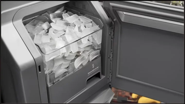 Open refrigerator freezer drawer showing built-in ice maker bin filled with crescent-shaped ice cubes ready for use.