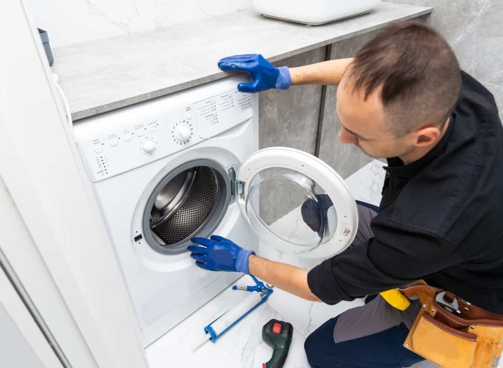 Plumber fixing washing machine on white background. High quality photo