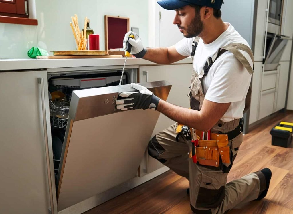 Service worker repairing dishwasher appliance in kitchen while use special tools. High quality photo