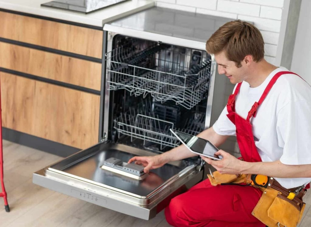 Repairman checks operating state of dishwasher in kitchen.