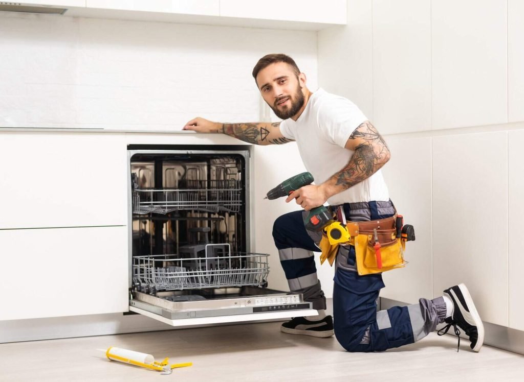 Young Repairman Service Worker Repairing Dishwasher Appliance In Kitchen.